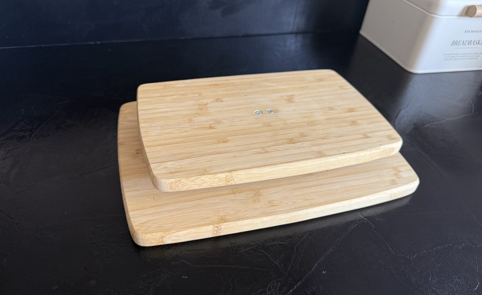 Top view of two stacked bamboo boards forming the scale platform, with two screw heads on the upper board where the load-cell beam is mounted underneath